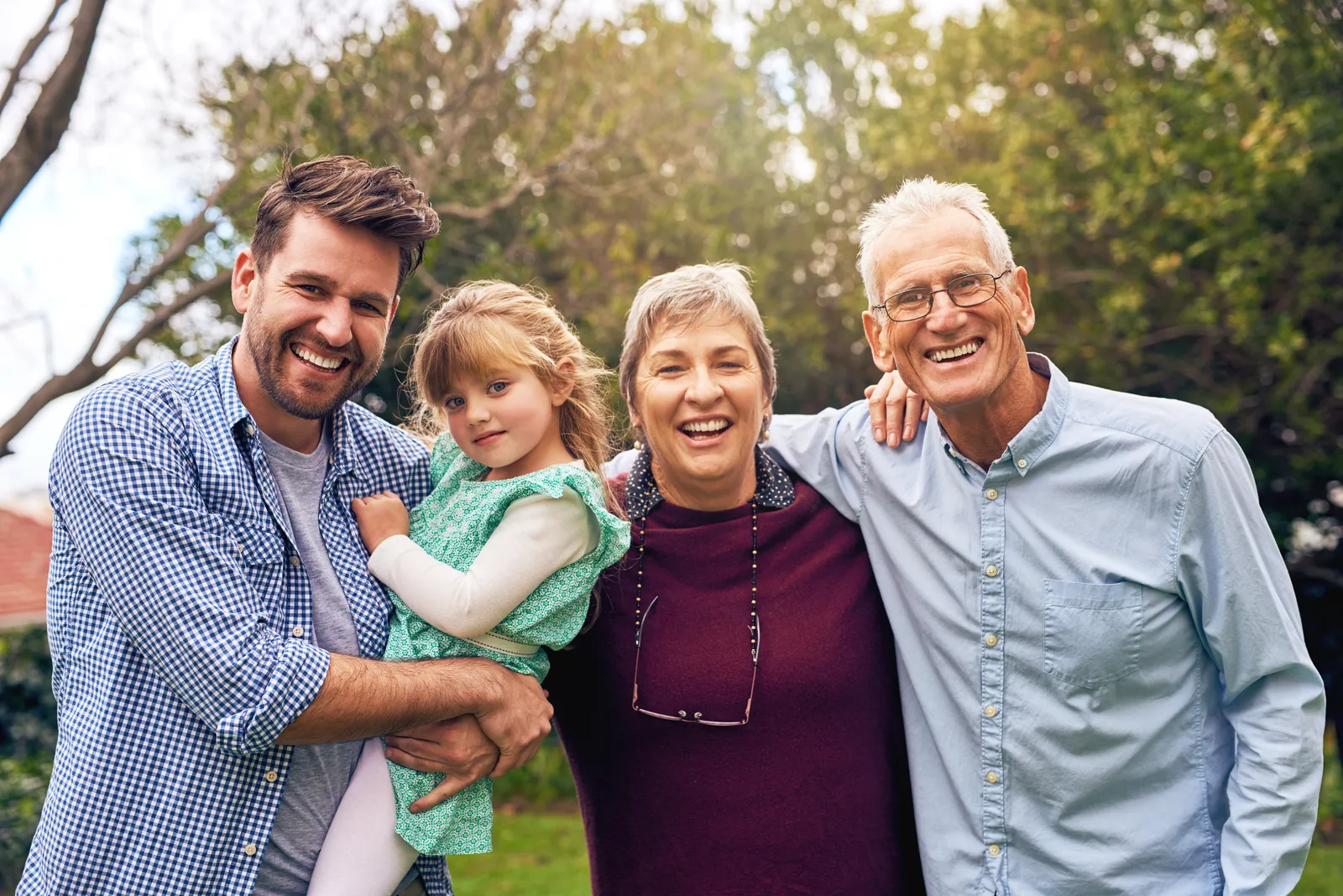Three generations of a family smiling together outdoors, man holding young girl.