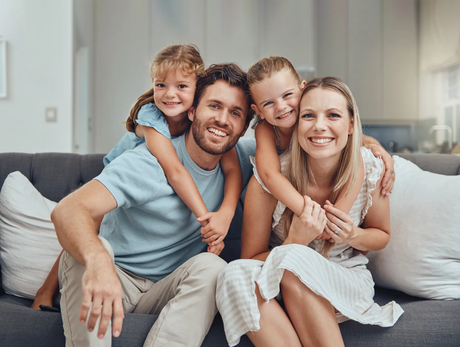 Family of four smiling together on a gray couch in a living room.