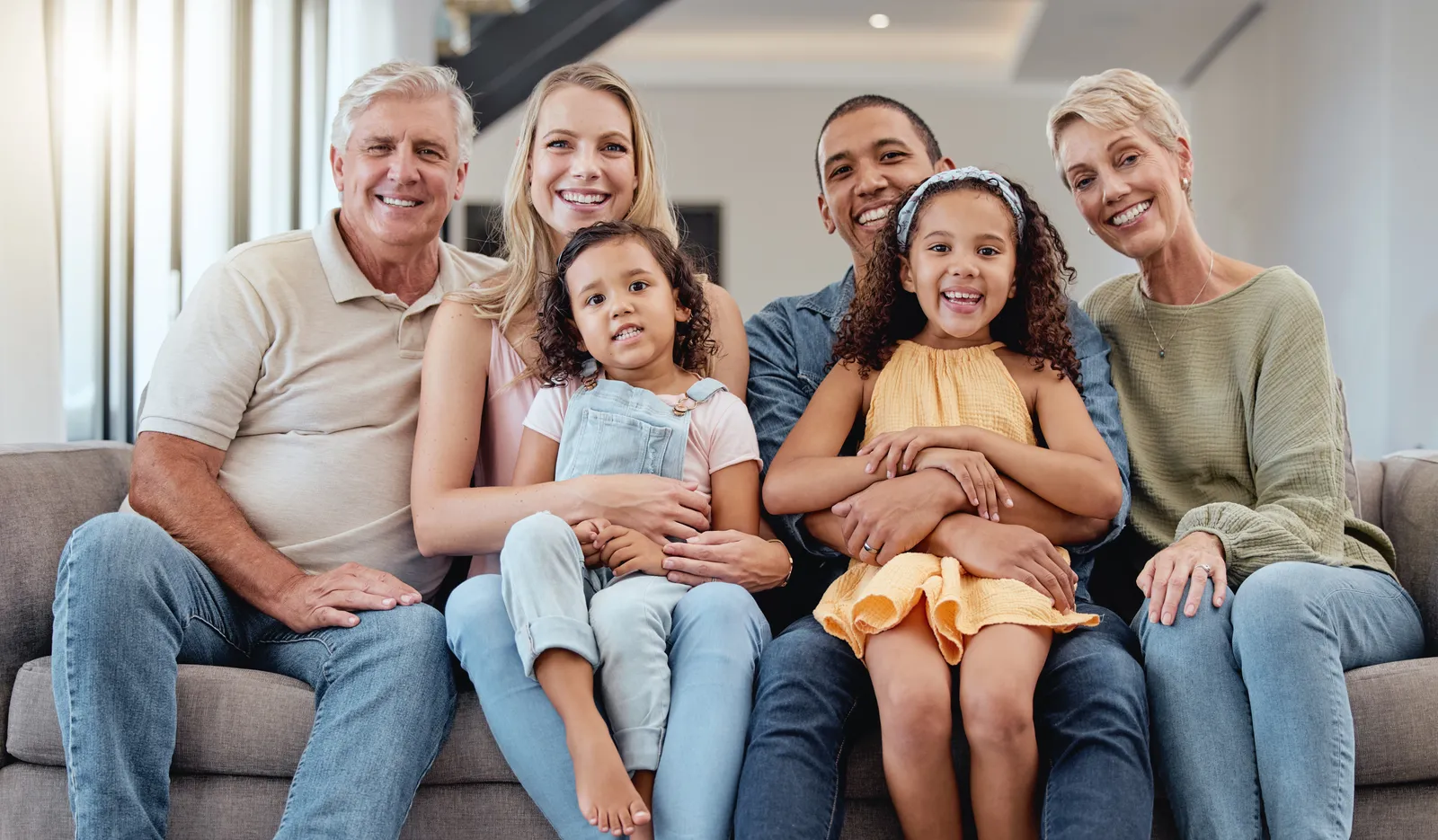 Three-generation family smiling together on a couch in a living room.